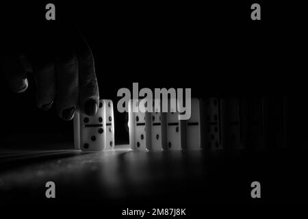 Main féminine et dominos sur la table dans la photo noir et blanc foncé, jouer des dominos Banque D'Images