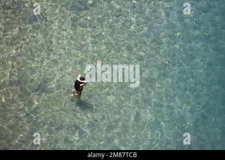 Vue aérienne sur la mer d'azur et femme qui va nager dans l'eau transparente. Vacances ensoleillées, vacances à la plage Banque D'Images