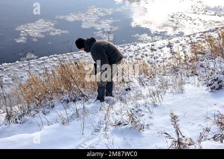 homme dans des vêtements chauds marchant dans la nature enneigée en hiver, se reposer, profiter d'un style de vie actif. un beau type recueille les herbes des champs enneigés. au niveau de la gelée Banque D'Images