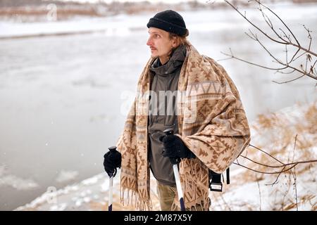 Portrait d'un homme d'âge moyen actif marchant dans une forêt naturelle enneigée en hiver. Beau gars en manteau foulard et chapeau regardant sur le côté, ayant le repos. Mois d'hiver Banque D'Images