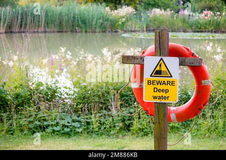 Signpost disant Beware Deep Water avec anneau de bouée de sauvetage dans le paysage de campagne au lac ou à l'étang Banque D'Images