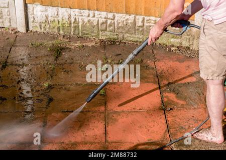 Un homme utilisant un nettoyeur haute pression pour nettoyer un patio sale avec un jet d'eau sous pression Banque D'Images