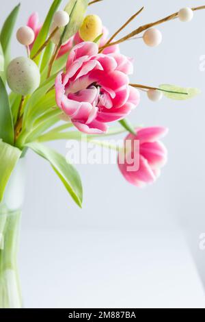 Bouquet frais de tulipes roses avec une branche d'oeufs de pâques sur fond blanc avec espace de copie Banque D'Images