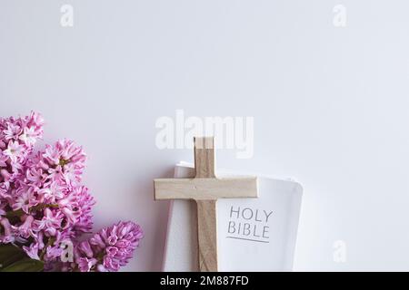 Bordure de la Bible chrétienne blanche, petite croix de bois et bouquet de fleurs de jacinthe rose sur fond blanc avec espace de copie Banque D'Images
