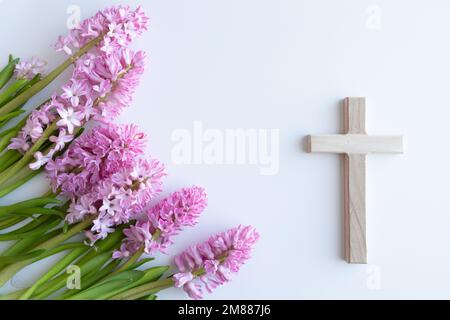 Simple croix chrétienne de bois sur fond blanc avec un bouquet de fleurs de jacinthe rose comme une bordure avec espace de copie Banque D'Images