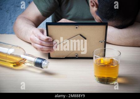 Triste mari ivre qui manque sa femme après le divorce avec une photo du couple qui est décédé au bar entouré de boissons à moitié finies Banque D'Images