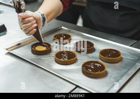 chef ajoutant du chocolat fondu dans un sac de tuyauterie aux biscuits cuits sur un plateau, processus de cuisson. Photo de haute qualité Banque D'Images