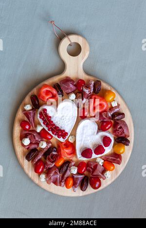 Plateau de fromages de la Saint-Valentin avec fromage en forme de coeur, charcuterie, tomates et fruits, vue de dessus Banque D'Images