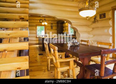 Escaliers en bois de pin blanc et table à manger en bois de cèdre avec chaises en rondins à haut dossier dans la salle à manger à l'intérieur de la maison en rondins de style scandinave. Banque D'Images