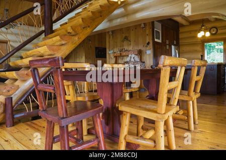 Table à manger en bois de cèdre avec chaises hautes dans la salle à manger et vue sur les escaliers en pin blanc à l'intérieur de la maison en bois de style scandinave, Québec, Canada. THI Banque D'Images