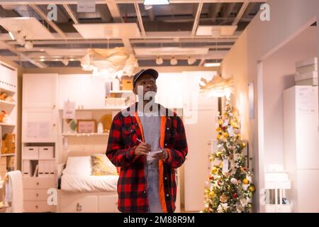 Homme ethnique noir qui fait du shopping dans un supermarché pour almeadas et coussins. shopping de noël Banque D'Images