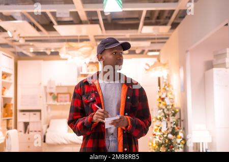 Homme ethnique noir qui fait du shopping dans un supermarché pour almeadas et coussins. shopping de noël Banque D'Images