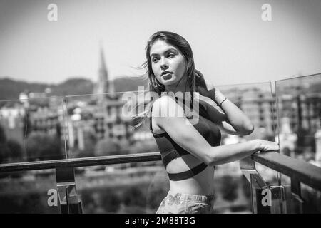 Portrait d'une jeune femme sur la terrasse d'un hôtel qui donne sur la ville depuis le haut, photo en noir et blanc Banque D'Images