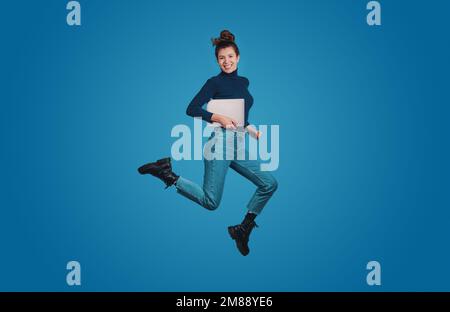 Profil de taille de corps pleine longueur de la femme positive excitée saut haute tenue cahier isolé sur fond bleu de couleur Banque D'Images