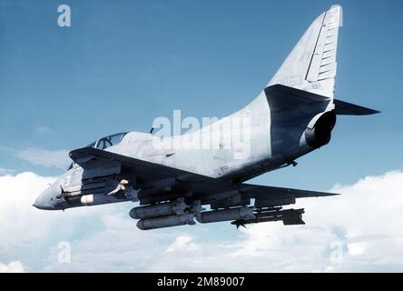 Vue aérienne à gauche d'un avion de l'escadron composite 10 (VC-10) TA-4J Skyhawk survolant une partie de la station navale de Guantanamo Bay (Cuba). L'avion est armé de missiles AIM-9 Sidewinder et de bombes à sous-munitions Mark 20. Pays : inconnu Banque D'Images