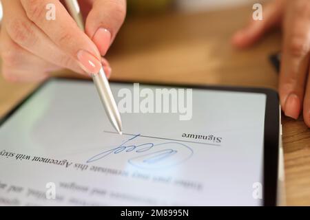 La main de la femme tient le stylet et fait la signature électronique dans le contrat sur la tablette. Banque D'Images