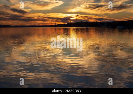 Coucher de soleil sur le lac Inks au parc national d'Inks Lake Texas USA. Le ciel brille tandis que les réflexions des nuages s'illuminent avec la lumière dorée qui projette des ombres. Banque D'Images