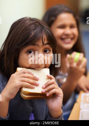 Manger le sandwich que ma mère a fait pour moi. Portrait d'une jeune fille d'école mangeant son sandwich à la cafétéria pendant le déjeuner. Banque D'Images