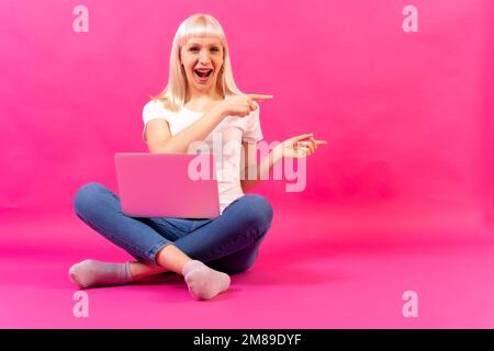 Portrait d'une femme blanche blonde avec un ordinateur sur fond rose Banque D'Images