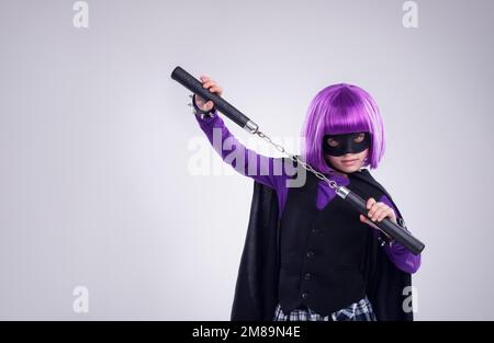 Petite fille, halloween et super-héros déguiser avec des nunchucks pour lutter contre un fond gris de studio. Portrait de fille isolée jouant super Banque D'Images