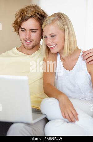 Profiter de leur connexion Internet rapide. Un jeune couple heureux utilisant un ordinateur portable ensemble dans leur salon. Banque D'Images