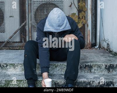 Un homme sans abri affamé et stressé, assis dans la rue de la ville, attend de l'aide et de l'argent. Banque D'Images