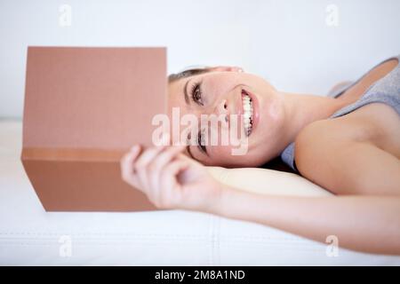 Un livre qui vous fait froid. Une jeune femme lisant un livre en étant allongé sur le canapé. Banque D'Images