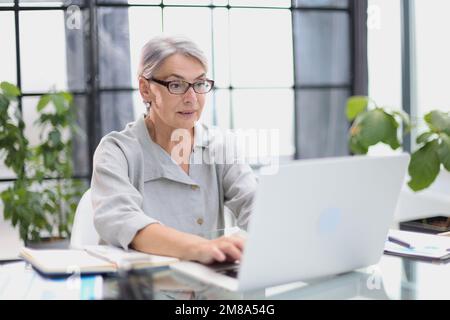 Une femme âgée et élégante travaillant avec un ordinateur portable au bureau. Banque D'Images