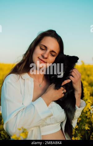 Une femme enceinte avec un petit chien noir dans la nature. Champ de colza Banque D'Images