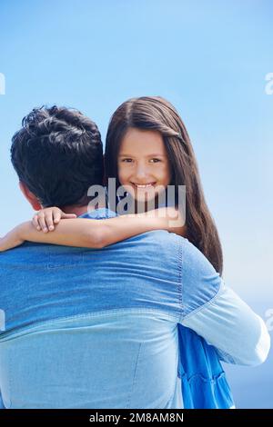 Fille de Daddys. Portrait d'une petite fille embrassant son père et souriant sur son épaule à l'appareil photo. Banque D'Images