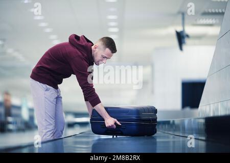 Voyager en avion. Le passager doit récupérer sa valise bleue dans la zone de retrait des bagages du terminal de l'aéroport. Banque D'Images