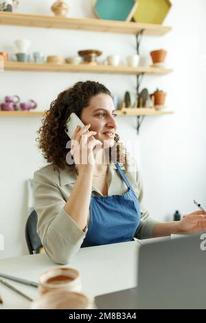 Femme céramiste lisant un message texte sur son smartphone. Femme d'affaires créative gérant un magasin avec une collection de produits céramiques. Entrée jeune Banque D'Images