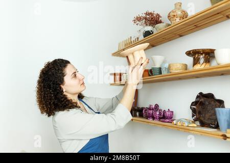 Jeune femme d'affaires dans son atelier est debout à côté de l'étagère avec des produits en céramique. Concept de démarrage de petites entreprises. Banque D'Images