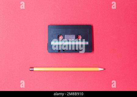 Une cassette compacte ancienne et un crayon sur fond rouge. Banque D'Images