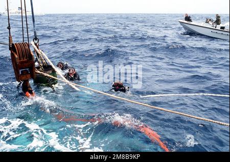 Les plongeurs du 1730th Pararescue Squadron regardent comme une grue à bord du navire de sauvetage japonais SHIN TATSU MARU élève un hélicoptère géant HH-3E Jolly Green de la Force aérienne à 1 800 pieds sous la surface. L'hélicoptère, qui s'est écrasé dans l'océan à 5,6 milles au large de la côte d'Okinawa, au Japon, est récupéré par une équipe de sauvetage conjointe États-Unis/Japon. Un grand navire de patrouille de classe Shiretoko de l'Agence japonaise de sécurité maritime, en haut à gauche, maintient la zone dégagée au fur et à mesure que l'opération progresse. Pays : Océan Pacifique (POC) Banque D'Images