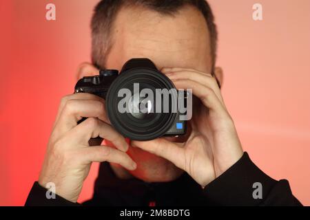 Un jeune prend une photo avec un appareil photo reflex numérique avec un ancien objectif sur fond rose Banque D'Images