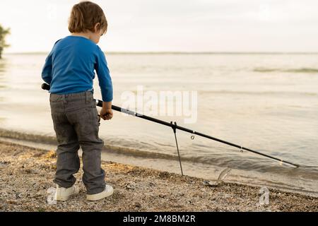 Adorable petit garçon sur la rivière avec pêche à la canne et pêche. petite pêche d'enfant sur le lac. bébé dans la nature Banque D'Images