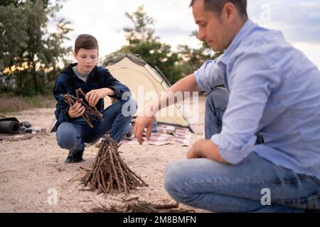 Père et fils passant du temps heureux de loisirs ensemble en plein air dans le camp. Famille homme enfant faisant feu de camp sur les bois de la nature. Relations bonheur activi Banque D'Images