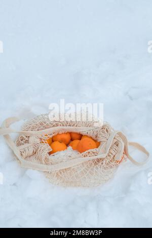 les mandarines dans un sac à ficelle ouverte reposent sur la neige. Pique-nique en hiver dans la forêt d'hiver Banque D'Images