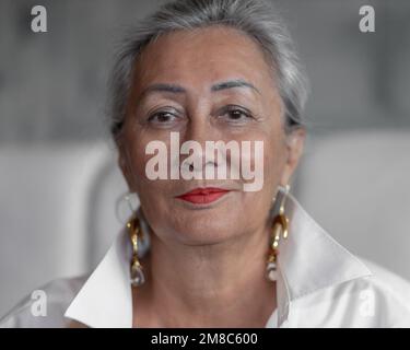 Portrait d'une belle femme mûre dans une chemise blanche, avec de longues boucles d'oreilles sur un fond clair Banque D'Images