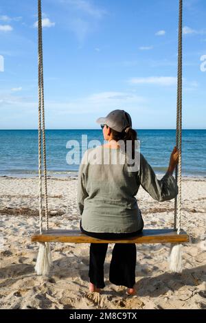 Femme assise sur une balançoire à la plage Banque D'Images