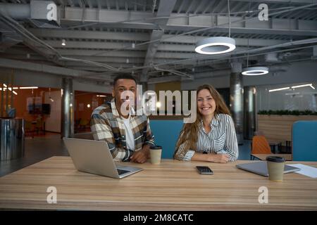 Des collègues heureux assis à la table dans le hall du bureau Banque D'Images
