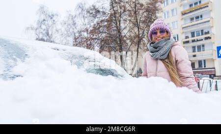 Bonne jeune femme de race blanche, en rose, à l'enragé de nettoyer la neige irst de sa voiture. Photo de haute qualité Banque D'Images