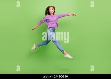 Photo pleine grandeur de jolie fille optimiste vêtue Jean violet pull-over sautant courir shopping isolé sur fond vert couleur Banque D'Images