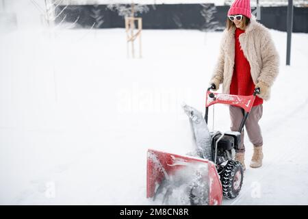 Une femme enlève la neige de la voie avec une fraise à neige Banque D'Images