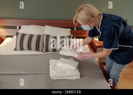 Housse de ménage dans le masque mettant une pile de serviettes de bain blanches sur le drap de lit. Concept de service d'étage Banque D'Images