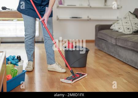 Femme méconnaissable lavant le sol avec une vadrouille dans le salon. Concept de nettoyage de maison professionnel Banque D'Images