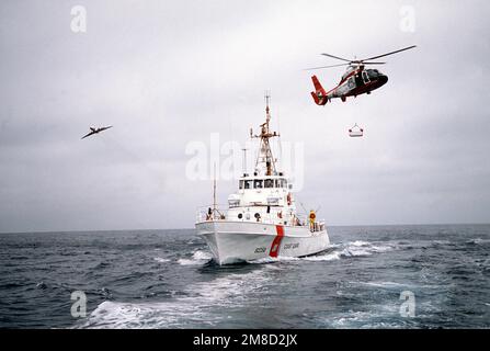 Un panier métallique est soulevé vers un hélicoptère Dophin HH-65A de la Garde côtière américaine après avoir transféré du matériel entre l'hélicoptère et le bateau de patrouille USCGC POINT STUART (WPB 82358) au cours d'une mission de routine. Un avion HU-25A Guardian est visible du côté tribord du navire. Pays : inconnu Banque D'Images