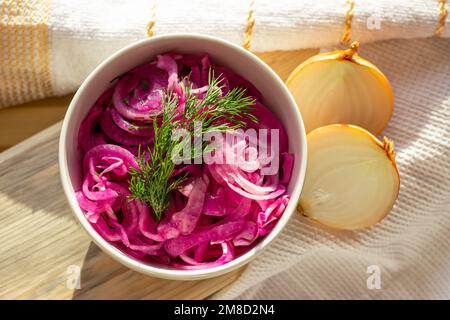 Délicieux oignons violets marinés marinés faits maison dans le bol blanc avec des bulbes d'oignon jaune dans la cuisine. Banque D'Images