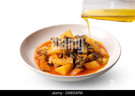 Des côtelettes de bettes de bettes suisses, cuites avec des pommes de terre et de la sauce tomate dans une assiette blanche avec de l'huile d'olive extra vierge versée sur la soupe isolée sur blanc Banque D'Images